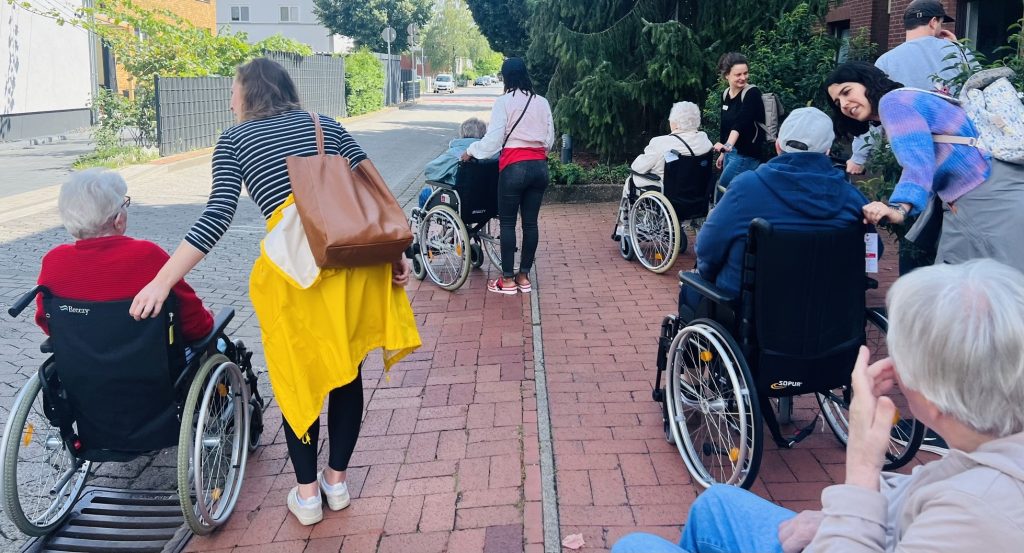 Begleite Senior*innen im Rollstuhl auf einem Spaziergang.